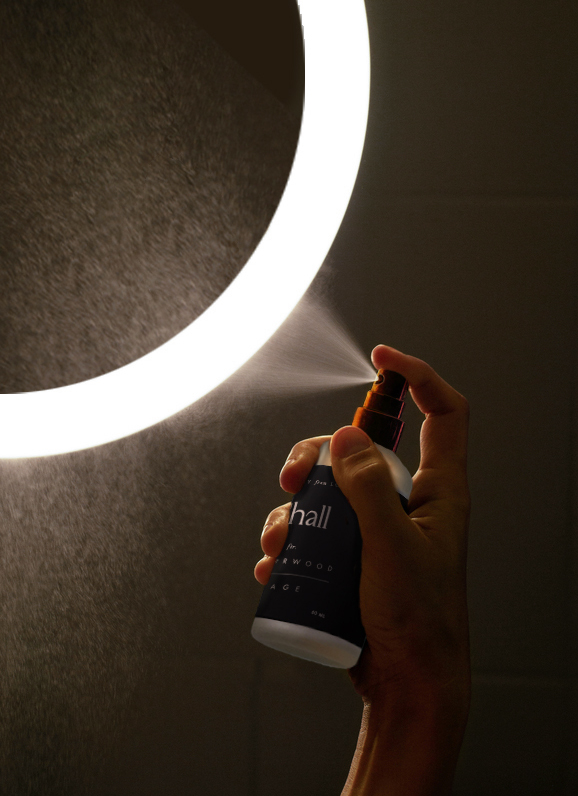 Young Woman Applying Thermal Water On Face Near Mirror In Bathroom.